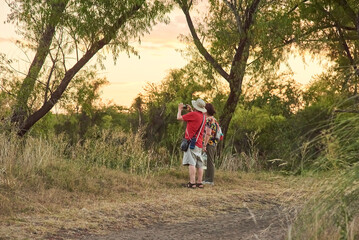 Fototapeta premium Couple of mature travelers taking pictures and enjoying the scenery at sunset at the Multiple Uses Natural Area, River of the Birds Park (Parque Rio de los Pájaros) in Colon, Entre Rios, Argentina.