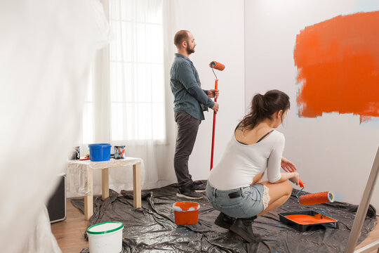 Family painting room with orange color paint to redecorate apartment with paintbrush and roller. Couple doing diy manual renovation using decorating tools and equipment, housework change.