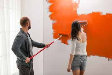Happy family painting with orange color, using paint to redecorate walls in apartment. Renovating house interior with paintbrush, renovation tools and roller, decorating room.