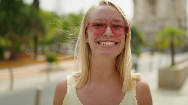 Young blonde woman smiling confident wearing heart sunglasses at park