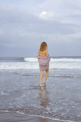 A young woman walks along the ocean at dawn, a time of meditation and reflection.