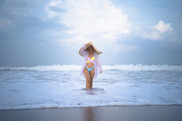 Young attractive woman in a big straw hat on the beach near the ocean. .Walk along the beach, have fun, vacation by the sea.