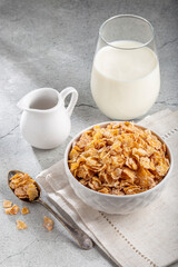 Corn flakes in bowl and glass of milk on table.