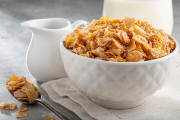 Corn flakes in bowl and glass of milk on table.