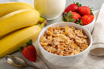 Corn flakes in the bowl with berries and milk on the table.