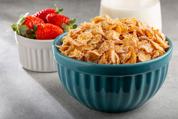 Corn flakes in the bowl with berries and milk on the table.