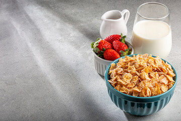 Corn flakes in the bowl with berries and milk on the table.