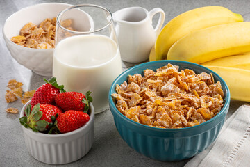 Corn flakes in the bowl with berries and milk on the table.