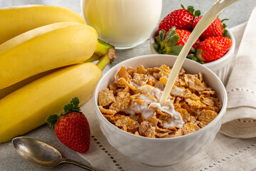Corn flakes in the bowl with berries and milk on the table.