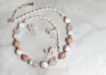 Necklace made of glass, porcelain and rose quartz beads and chestnut flowers, composition with women's jewelry, selective focus, horizontal orientation.