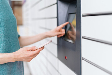 Woman standing near automatic post terminal with smartphone