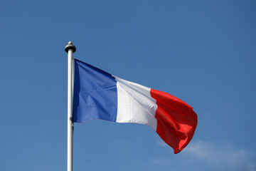 French flag flying in the wind with blue sky background.  Flag of France, the Tricolor on a White flagpole,