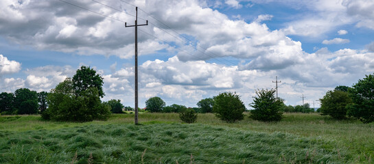 krajobraz linii elektrycznej pośrodku zielonych pól w zachodniej Polsce, jasne zielono niebieskie kolory lekko pochmurna pogoda - obrazy, fototapety, plakaty