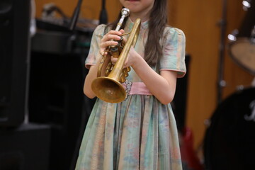 A little girl young musician trumpeter playing trumpet concert standing on stage alone holding...