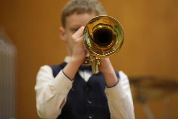A little musician with a trumpet plays a concert a view of the bell of a musical instrument a close-up image of a blowing trumpeter in front - obrazy, fototapety, plakaty