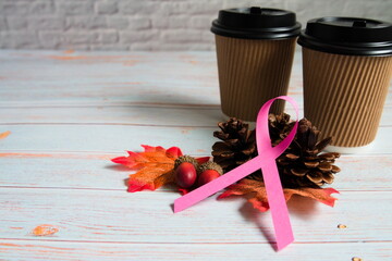 ピンクリボンと紙カップと松ぼっくりとどんぐりと紅葉と木製背景の右寄りの写真