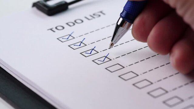 Checklist and To Do List Concept. Close-up businessman tick off or marking with blue pen on checklist, checkbox, to do list box after completing task on white paper. Selective focus 4K resolution