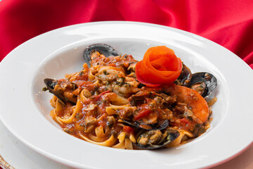 Pasta macarrão italiano em prato branco com fundo vermelho com camarão, lagosta, ostras, bonito, com molho de tomate, com flor de tomate