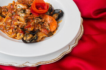 Massa fettuccine com molho de frutos-do-mar, mediterrâneo com flor de tomate em prato branco e toalha vermelha tipico italiano