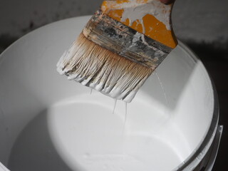 White paint dripping from a brush into a jar