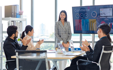 Businesswoman manager presenter in formal suit standing holding pen pointing at graph chart document on whiteboard presenting company information to Asian male female colleagues in meeting room