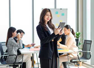 Portrait shot millennial Asian cheerful successful professional businesswoman entrepreneur in formal suit standing smiling crossed arm holding tablet computer in meeting room while employee working