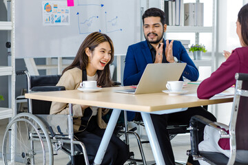 Millennial Indian male businessman manager mentor in formal suit talking helping disabled handicapped female employee sit on wheelchair working with laptop computer on table in office meeting room - obrazy, fototapety, plakaty