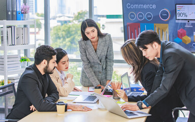 Businesswoman manager presenter in formal suit standing holding pen pointing at graph chart document on whiteboard presenting company information to Asian male female colleagues in meeting room