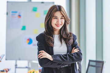 Portrait shot of millennial Asian cheerful successful professional businesswoman entrepreneur in formal suit standing smiling crossed arms in meeting room while employee and colleague brainstorming