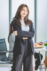 Portrait shot millennial Asian cheerful successful professional businesswoman entrepreneur in formal suit standing smiling crossed arm holding tablet computer in meeting room while employee working