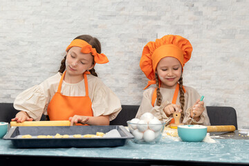 Happy family. Funny girls kids in orange chef uniform are preparing the dough, bake cookies in the kitchen. Sisters children enjoy cooking food. Warm relations.