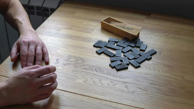 Male hands are taking seven dominoes on the background of wooden table. Preparing to play dominoes