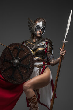 Shot of female warrior from past with shield and spear dressed in armor and red cape looking at camera.