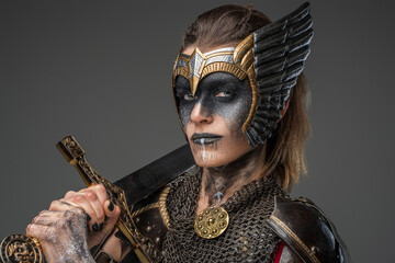 Shot of valkyrie dressed in ancient dark armor holding sword on her shoulder.