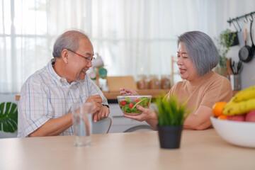 Senior couple eating salad together at the kitchen at home. Concept of healthy nutrition in older age.