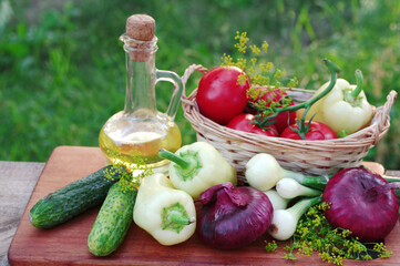 A variety of vegetables and a bottle of sunflower oil on a cutting board on a natural background.