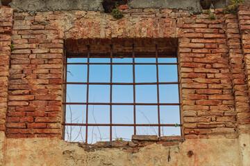 Vecchia finestra, che guarda sul cielo azzurro, sbarrata e su muro rosso di mattoni di vecchio edificio.