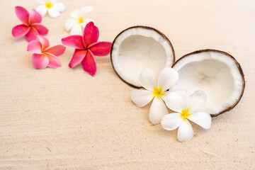 Coconut fruit and frangipani flowers on sand beach background.