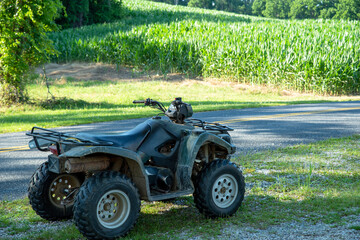 Fototapeta premium Green off-road vehicle in foreground with sunny agricultural cornfield and woods beyond with no people and copy space.