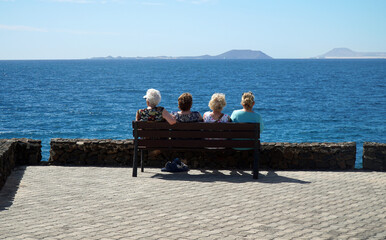 Four older ladies sitting on bench   looking at view across sea to  Fuerteventura