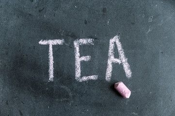 Tea. A word written in pink chalk on a black chalkboard. Handwritten text. A piece of colored chalk hangs next to it.