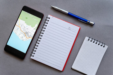 Two notebooks, smartphone and pencil on gray. A map of the city of Santa Barbara on the screen of...