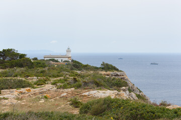 Fototapeta na wymiar Lighthouse at Far de Cap Blanc in Mallorca, Spain. Naval ships in sea in background