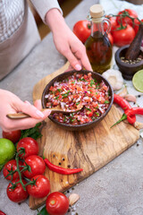 making salsa dip sauce - woman mixing chopped ingredients in wooden bowl