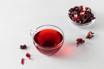 Herbal tea made from hibiscus petals in a transparent cup and a bowl of dry hibiscus.