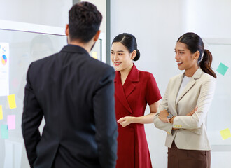 Fototapeta na wymiar Asian young beautiful professional successful businesswoman standing smiling holding hand presenting showing graph chart report data paperwork documents on glass board to male and female colleagues