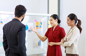 Asian young beautiful professional successful businesswoman standing smiling holding hand presenting showing graph chart report data paperwork documents on glass board to male and female colleagues