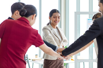 Millennial Asian young beautiful professional successful businesswoman in formal suit standing holding hands with male and female colleagues showing unity and success teamwork in company meeting room.