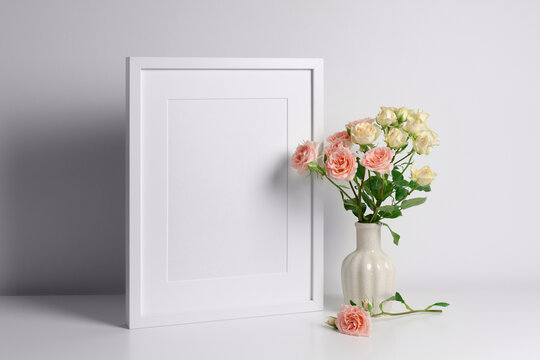 Portrait frame mockup in white interior and fresh roses bouquet, mockup for artwork or paintings