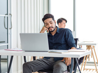 Indian stressed depressed exhausted bearded male businessman sitting at workstation with laptop...